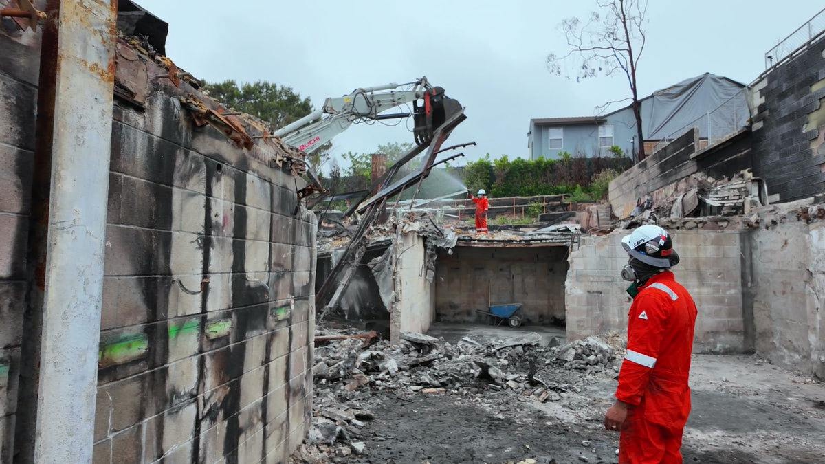 Workers and an excavator clearing debris at a fire-damaged site